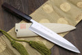 Japanese chef knife with light saya, dark handle, and green cord