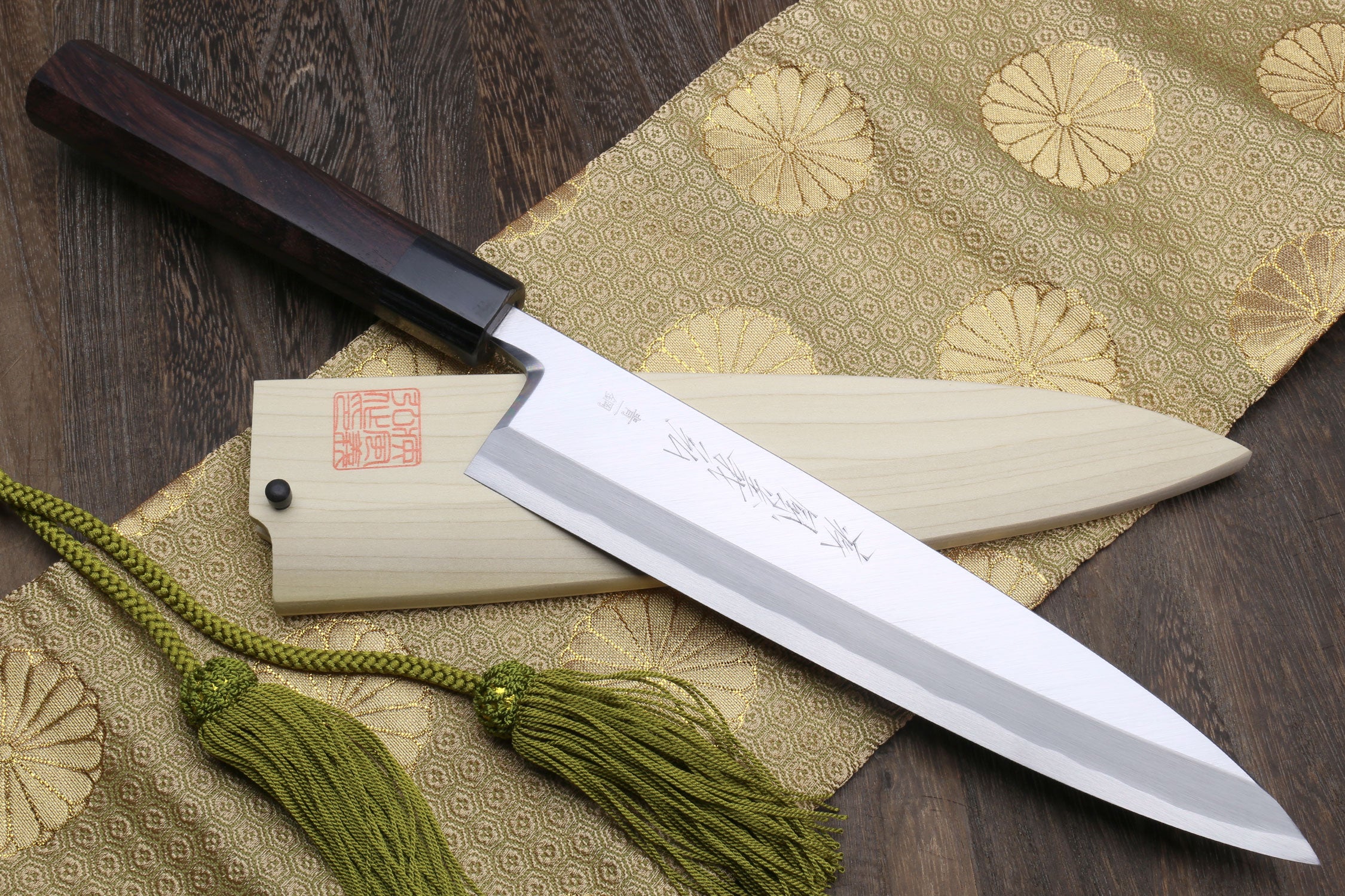 Japanese chef knife with light saya, dark handle, and green cord