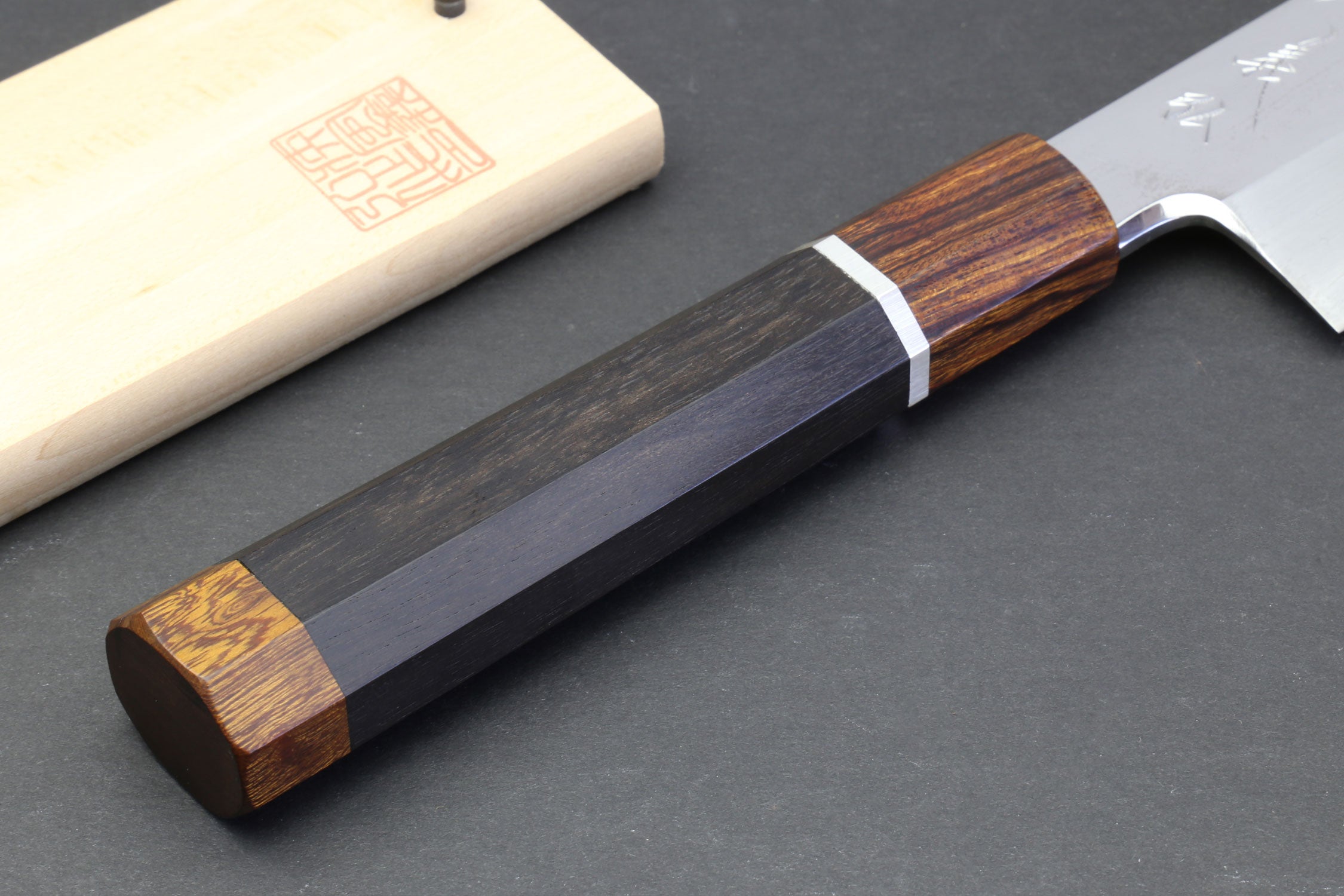 Japanese chef knife with mirror-polished blade and dark handle, wooden sheath nearby