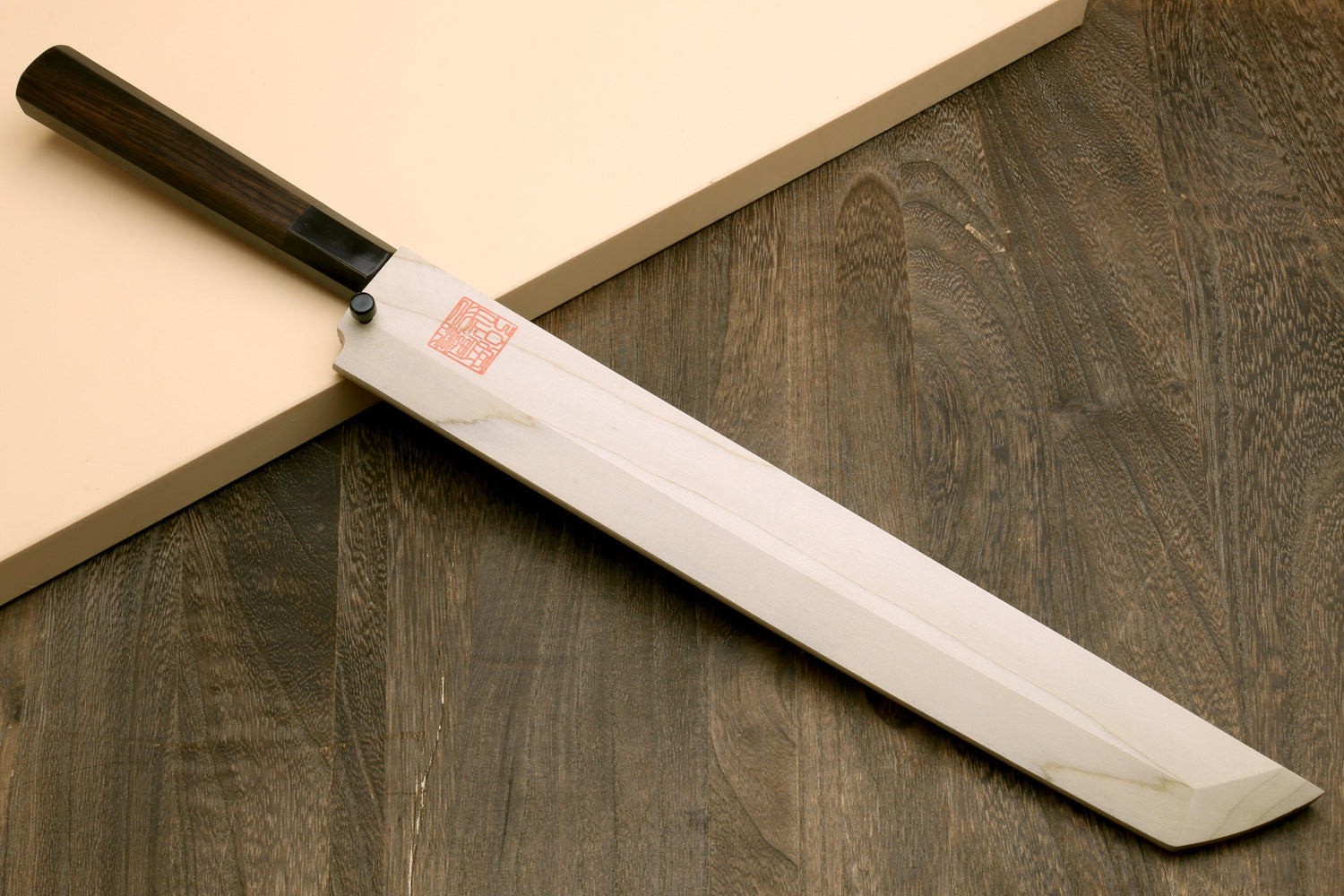 Japanese slicing knife with pale steel blade and dark handle on wooden boards