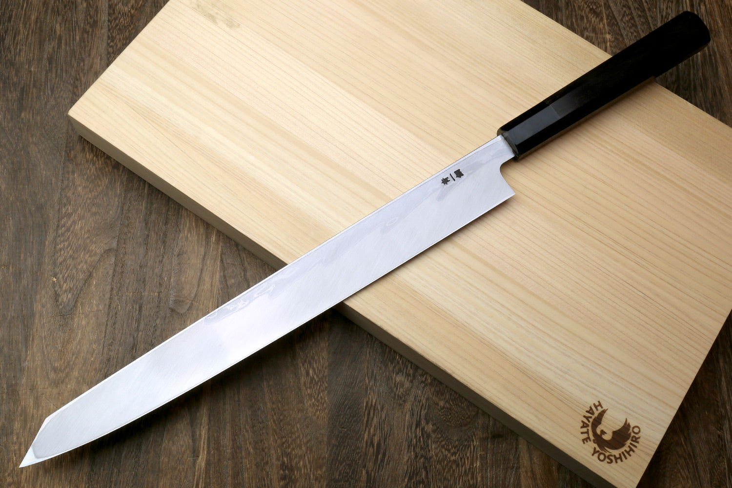 Japanese sushi knife with long wavy blade and black ebony handle on stand.
