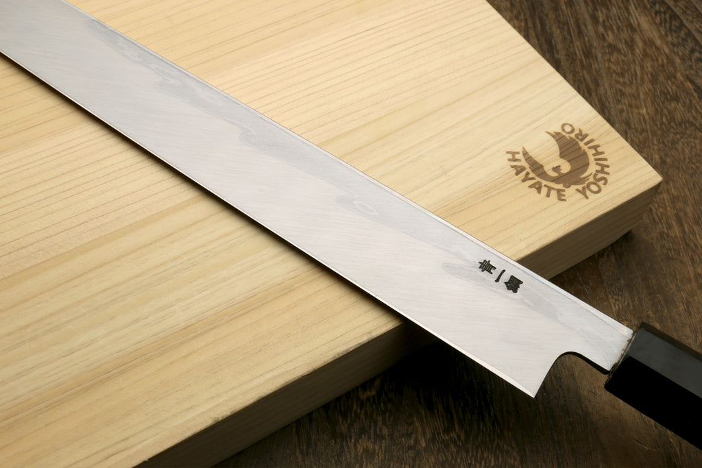 Japanese sushi knife laid on wood, showing wavy blade and ebony handle.