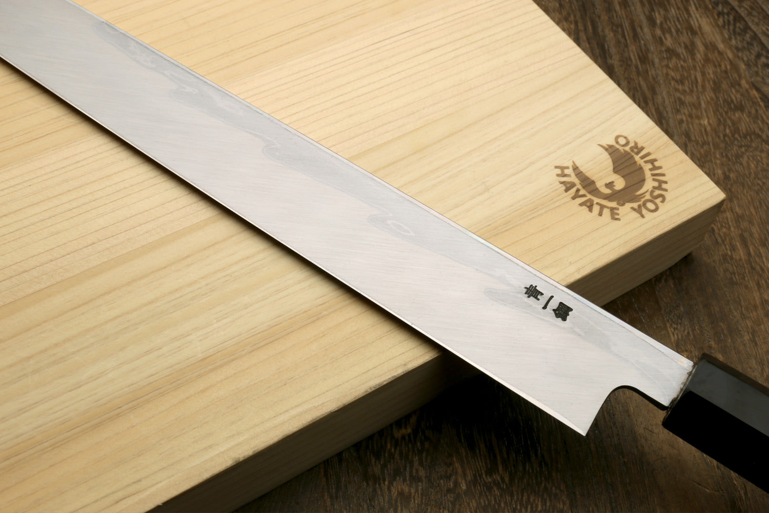 Japanese sushi knife laid on wood, showing wavy blade and ebony handle.