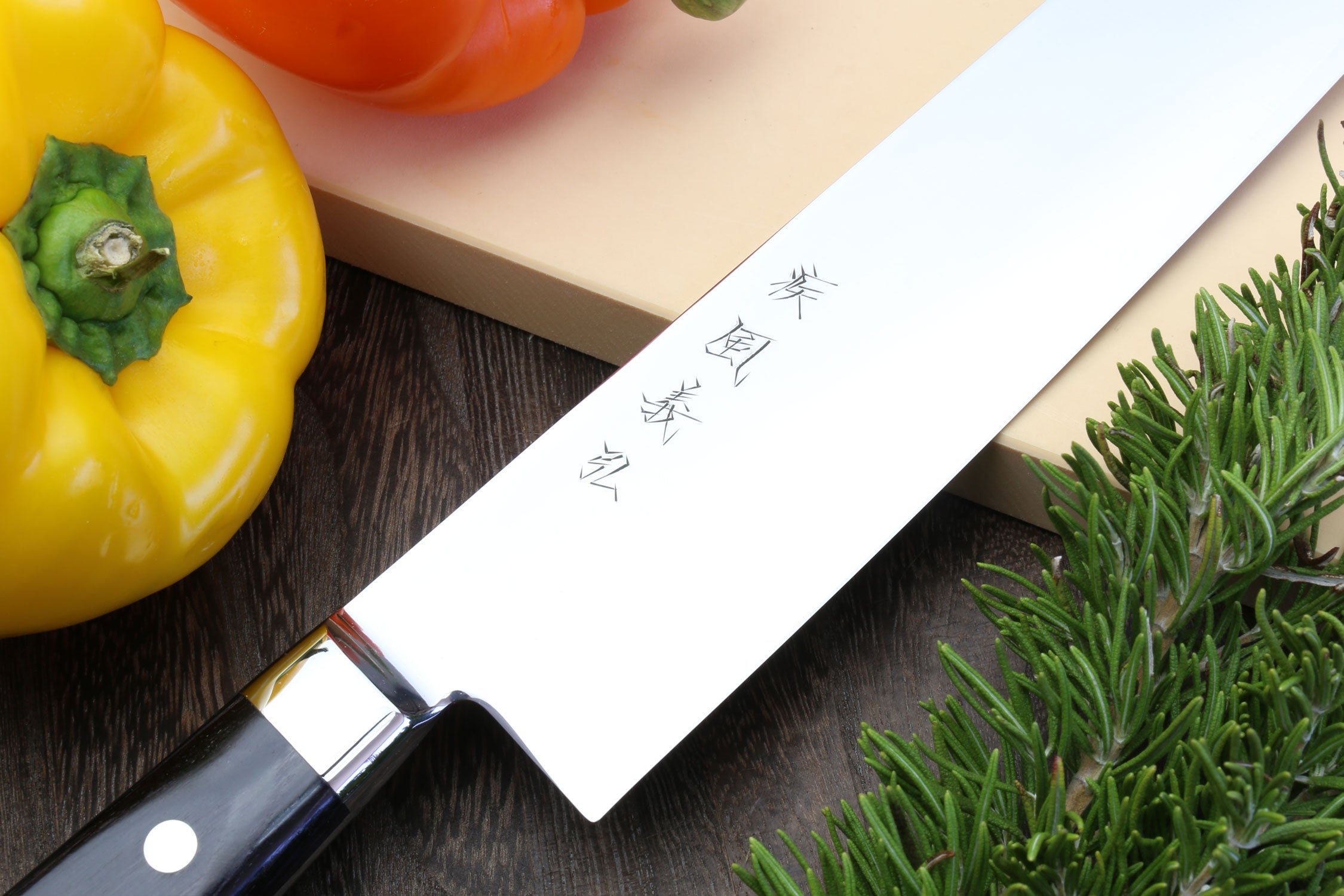 Kiritsuke chef knife close-up: silver blade with etched marks and black pakkawood handle