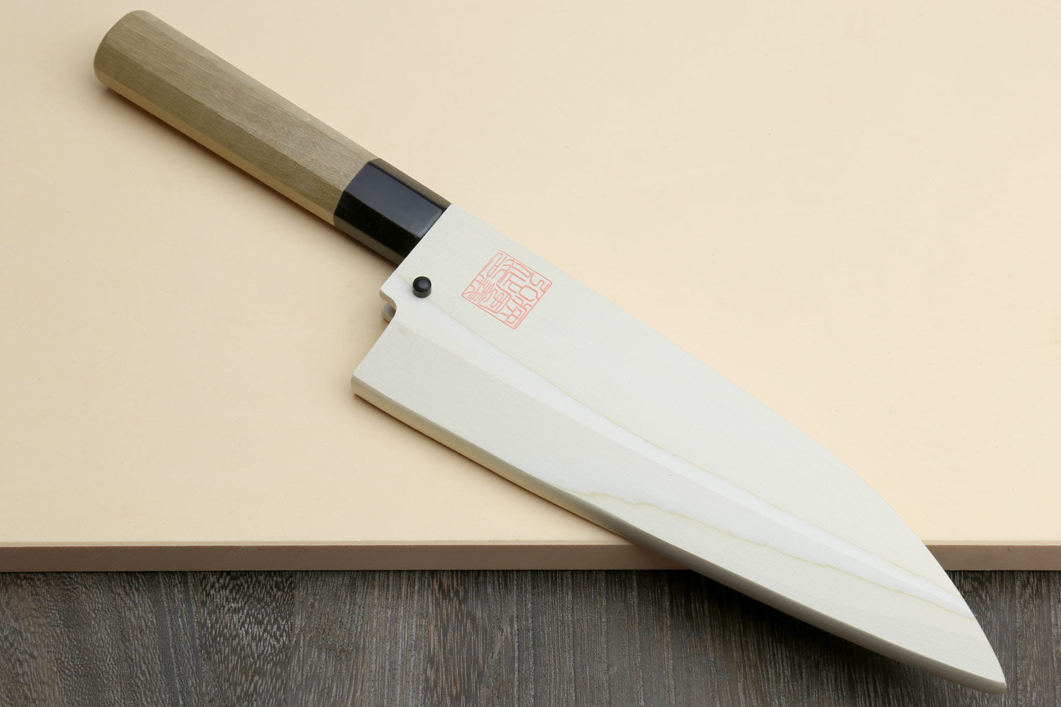 Deba chef knife on board with white blade, light wood handle, and black bolster