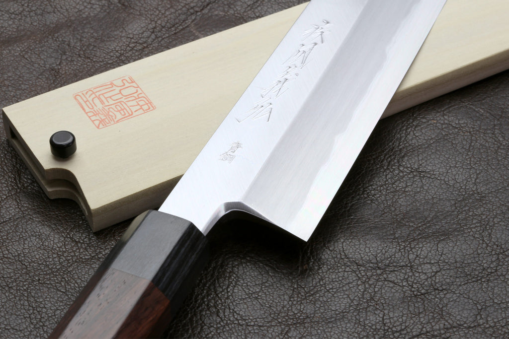 Japanese chef knife with pale blade and saya, dark handle, on leather