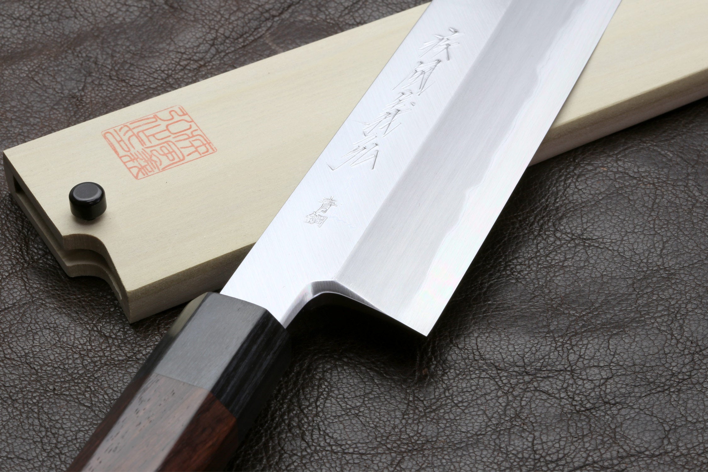 Japanese chef knife with pale blade and saya, dark handle, on leather