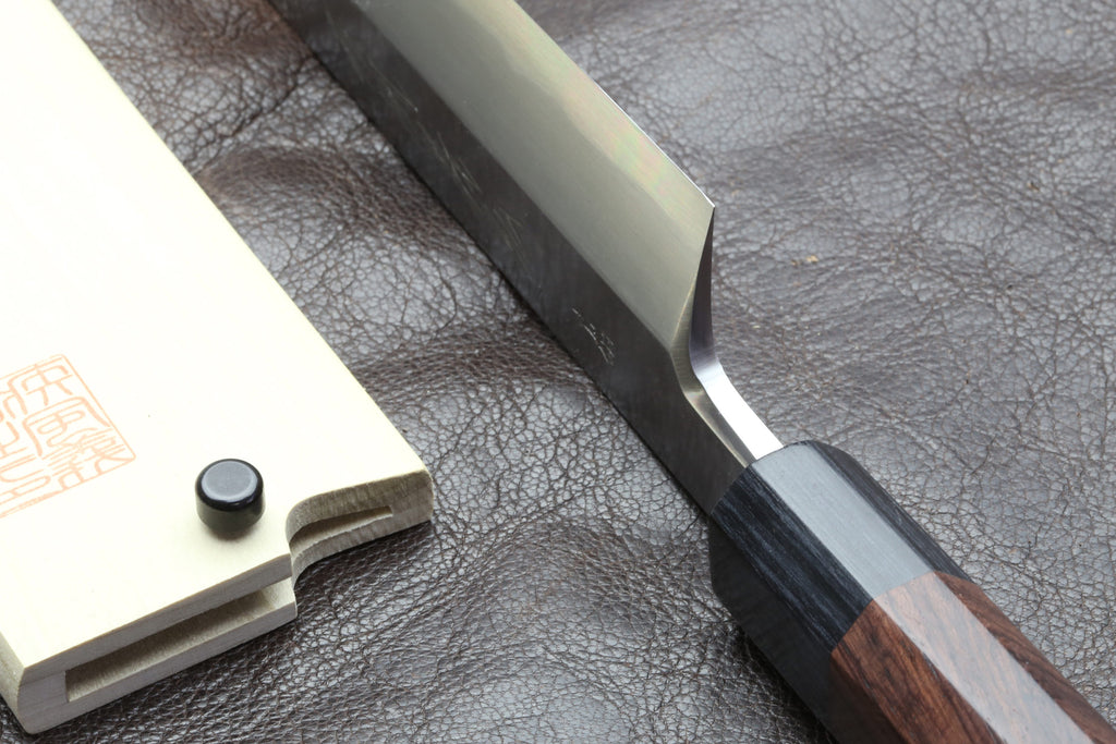 Japanese chef knife tang and blade base close-up with dark handle on leather