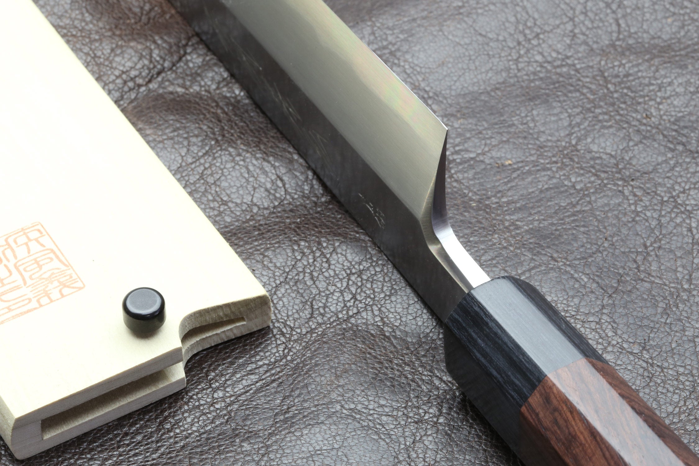 Japanese chef knife tang and blade base close-up with dark handle on leather