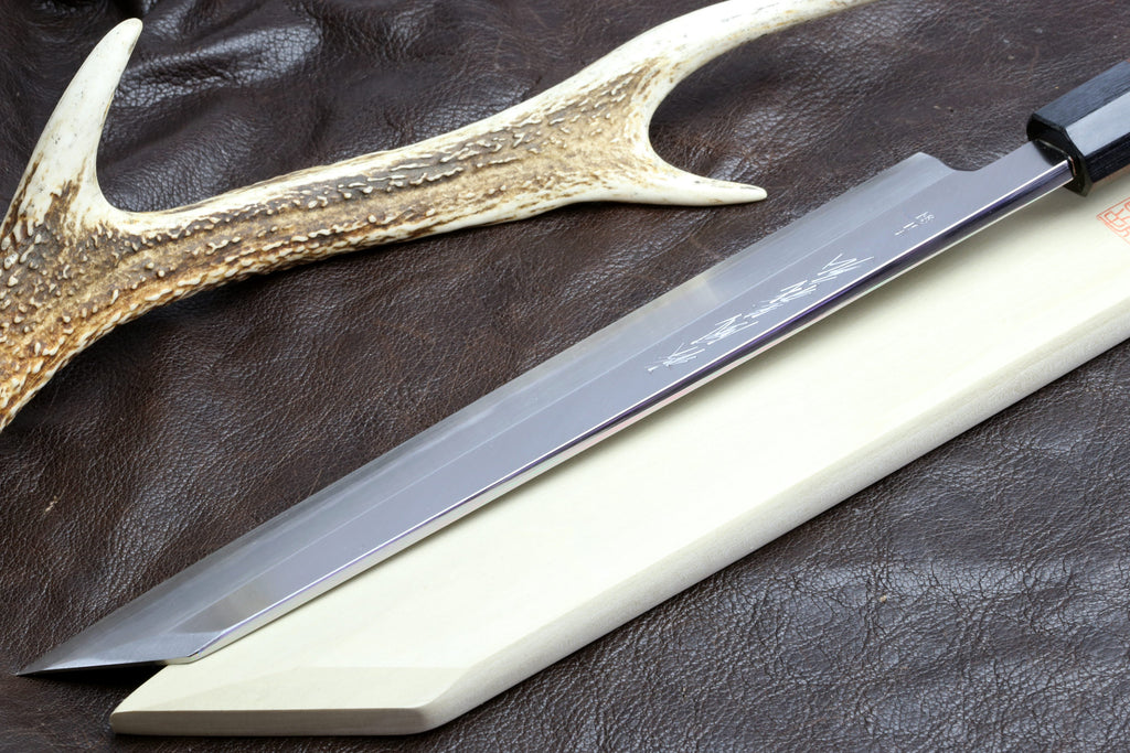 Japanese chef knife close-up: pale blade and dark handle, antler-style guard nearby