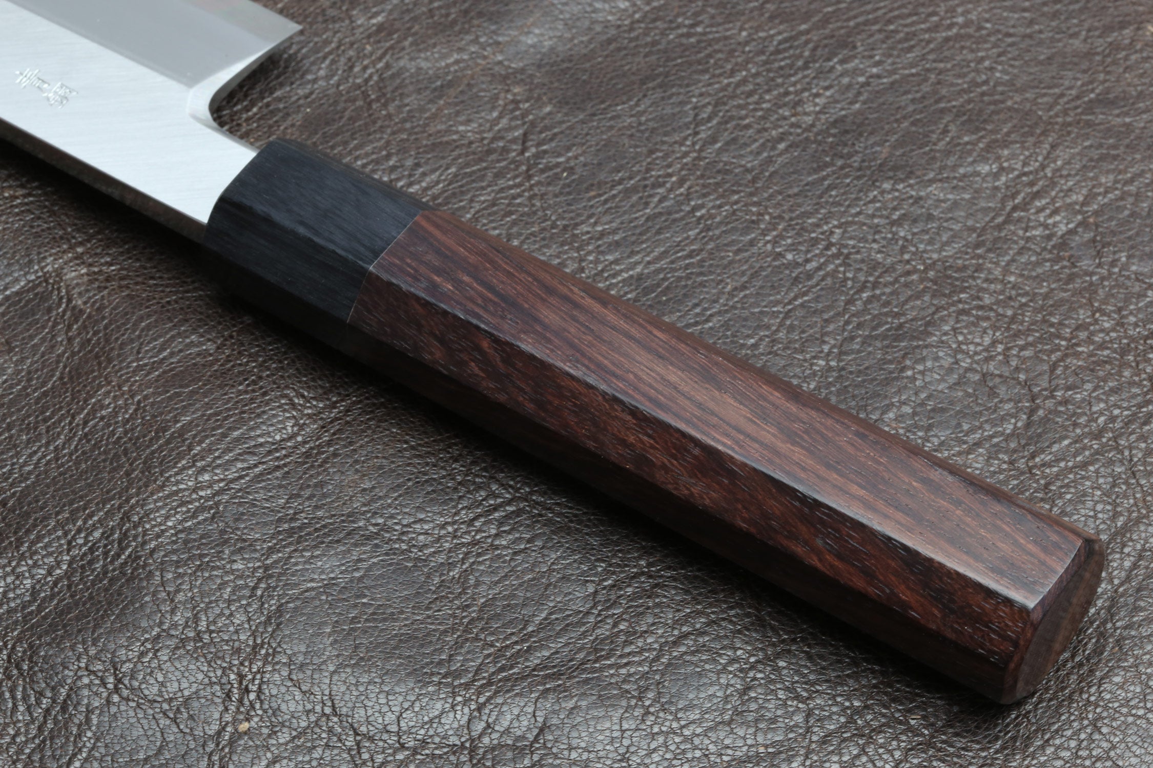 Knife handle close-up with dark brown wood grain and dark end cap on leather
