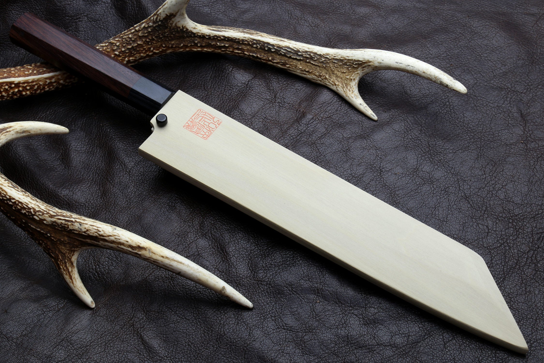 Japanese chef knife with pale blade and dark handle, angled on dark leather