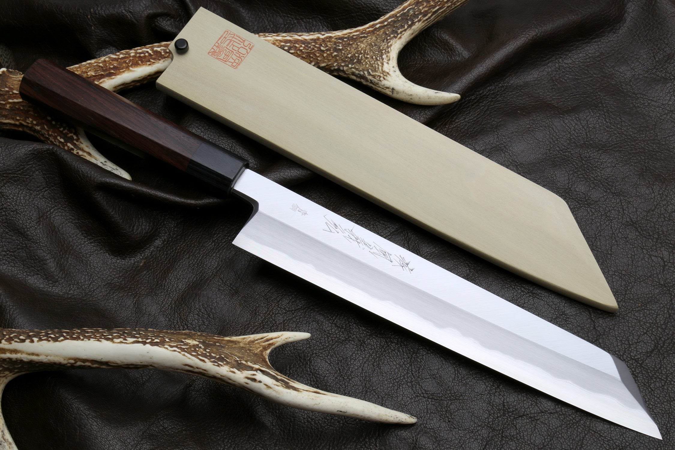 Japanese chef knife with pale blade, dark handle, and antler-style sheath on leather