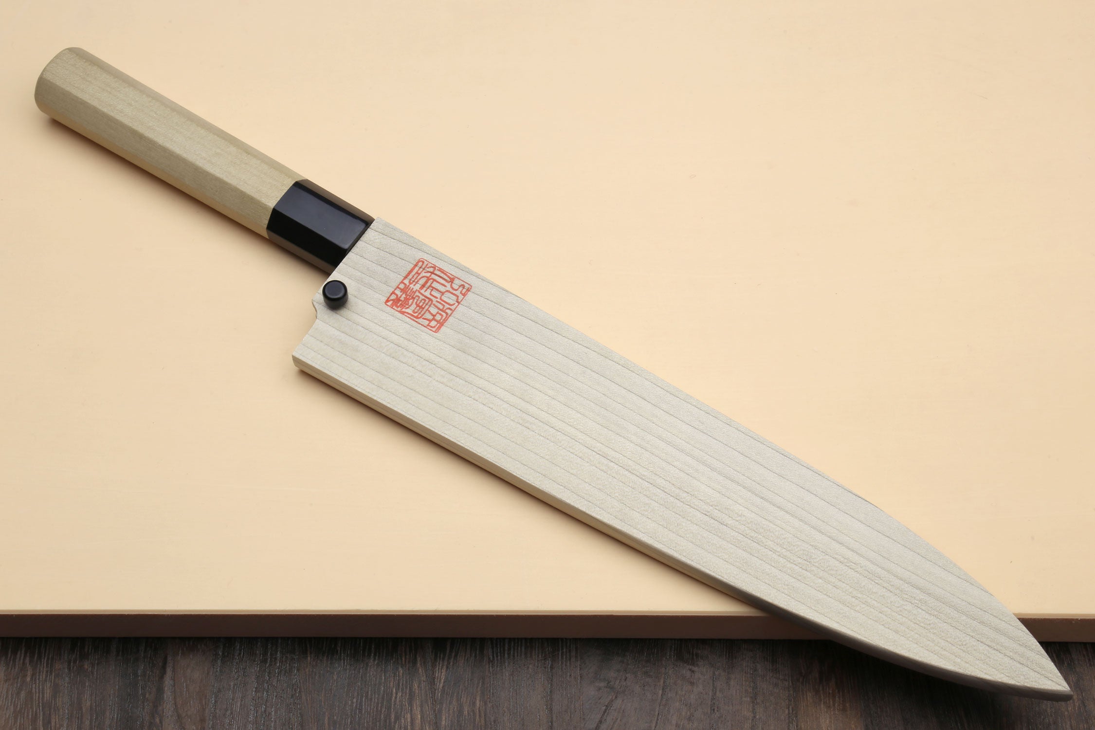 Japanese sushi knife with light wood handle, black collar, and silver blade on board