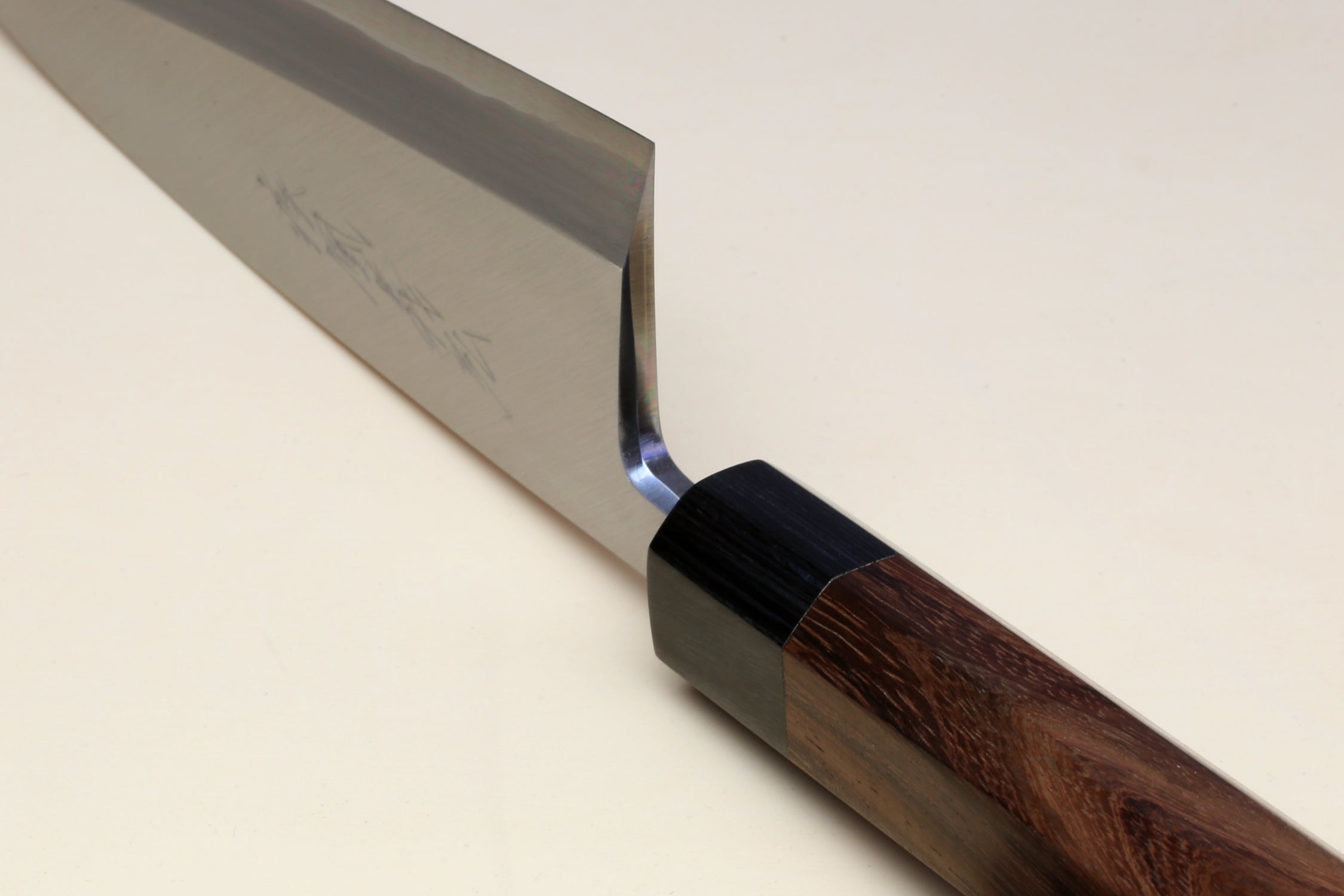 Deba fish fillet knife angled close-up, silver blade with dark bolster and rosewood grip