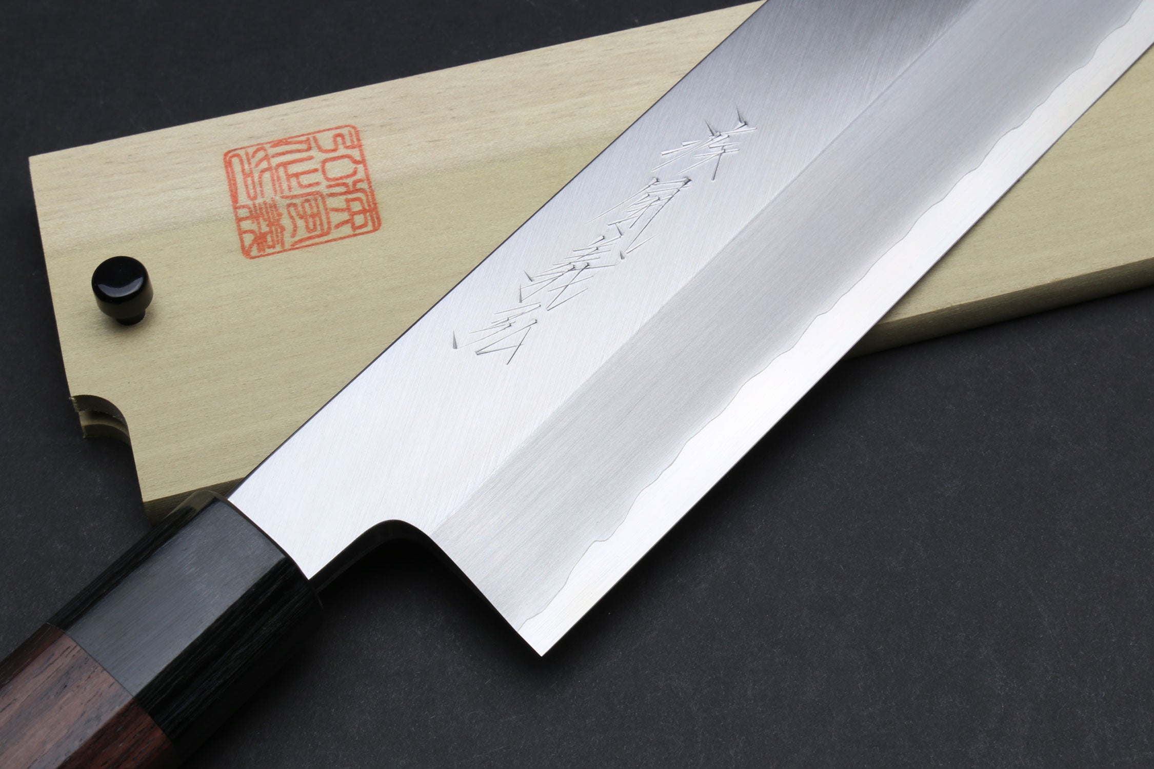Japanese chef knife blade close-up with pale saya and dark bolster
