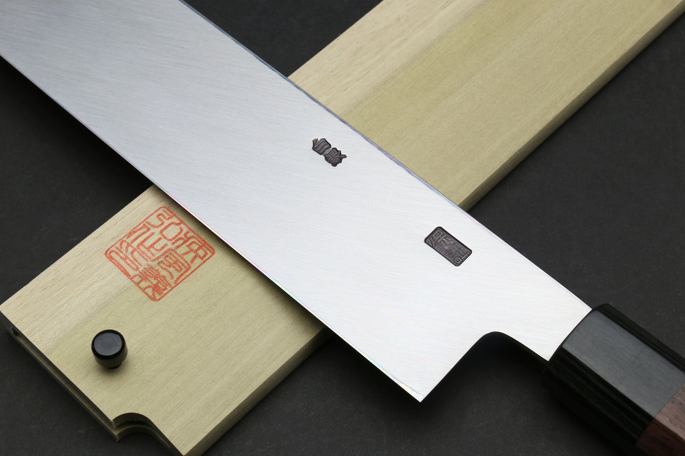 Japanese chef knife front view with dark handle, black bolster, and pale saya