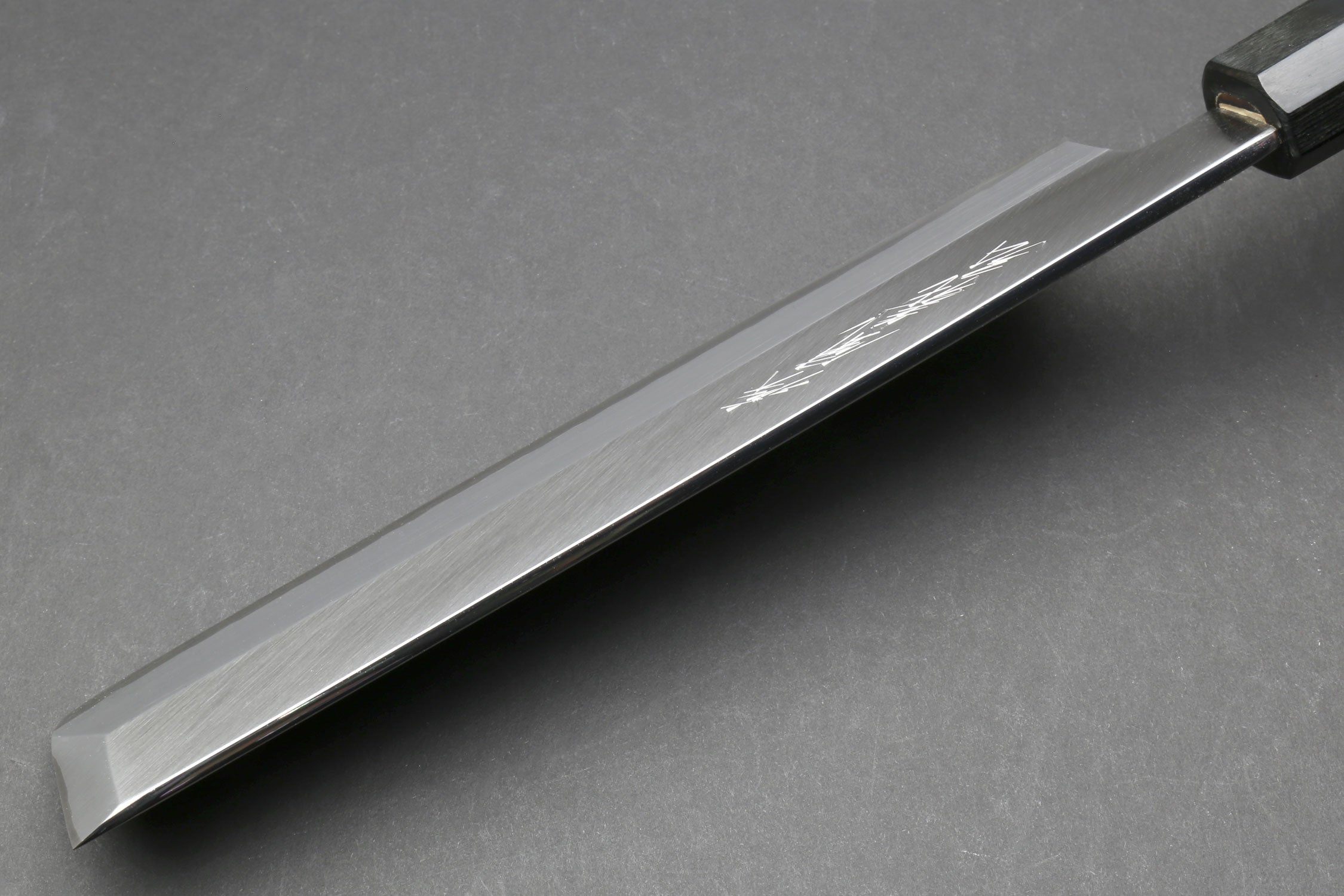 Japanese chef knife blade close-up with polished edge and dark bolster