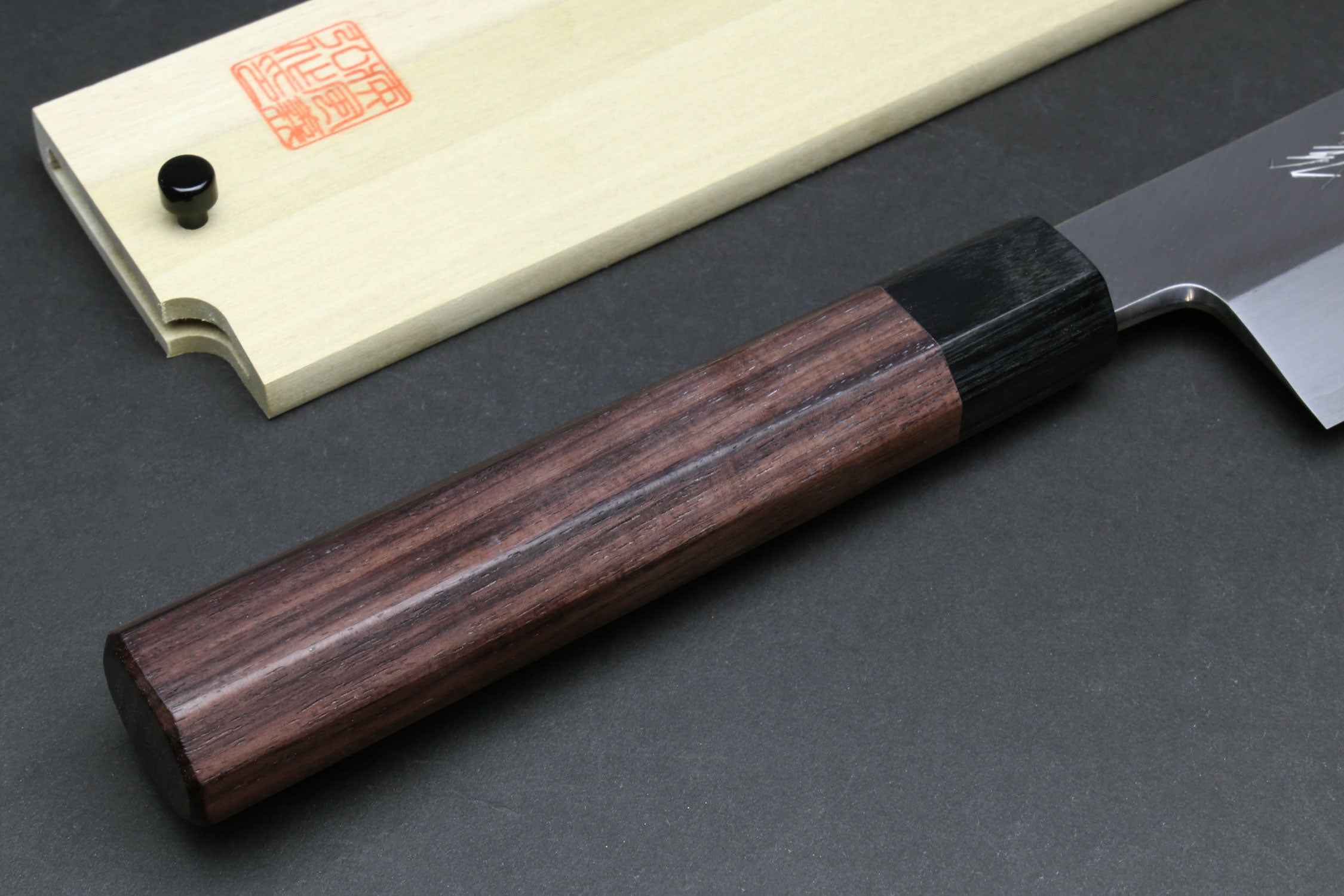 Japanese chef knife wooden handle close-up with dark bolster and pale saya