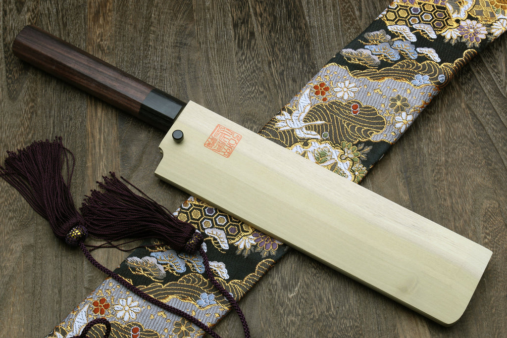 Japanese chef knife with light saya, dark handle, and tassel cord
