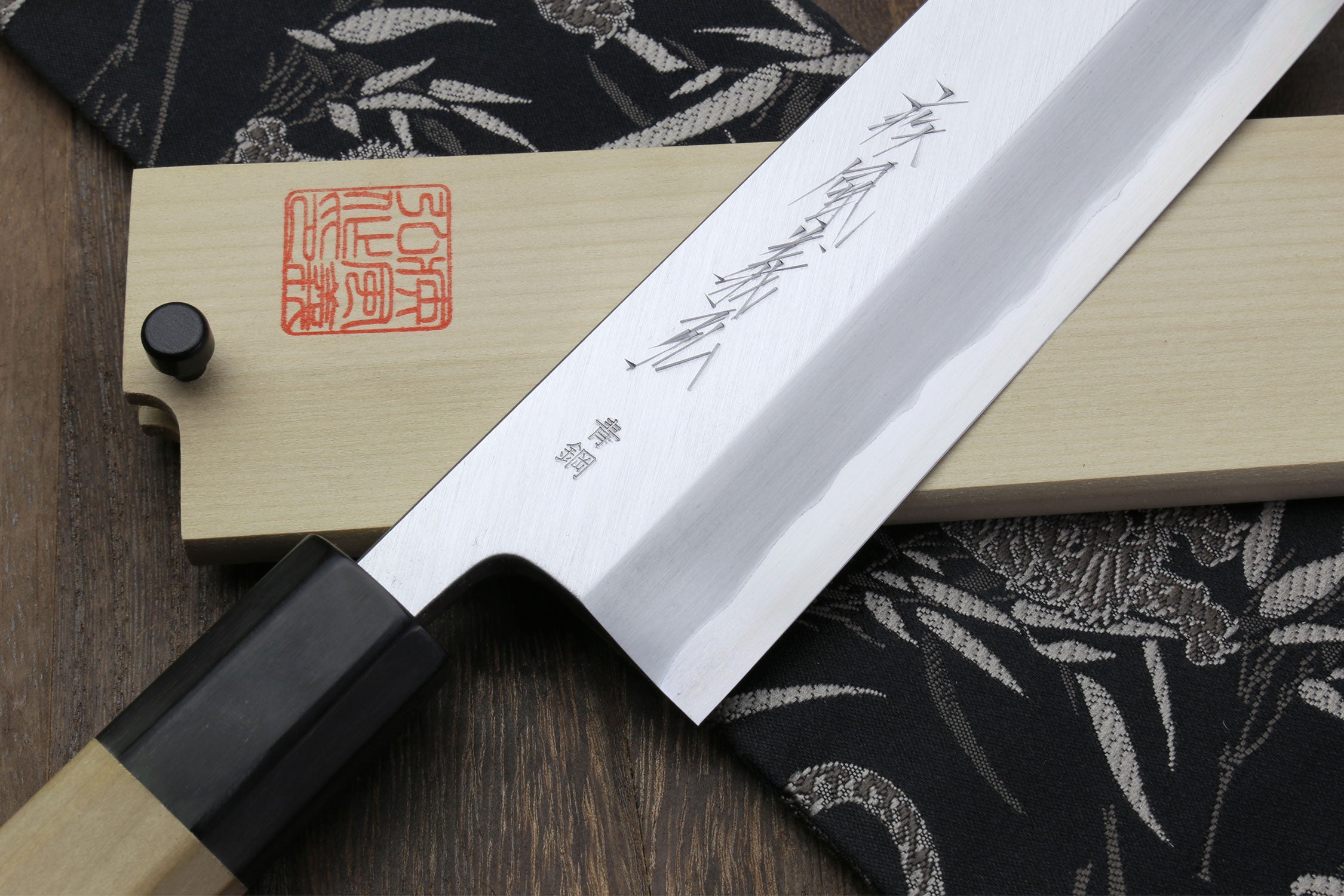 Eel filet knife blade with etched markings and light saya on patterned cloth