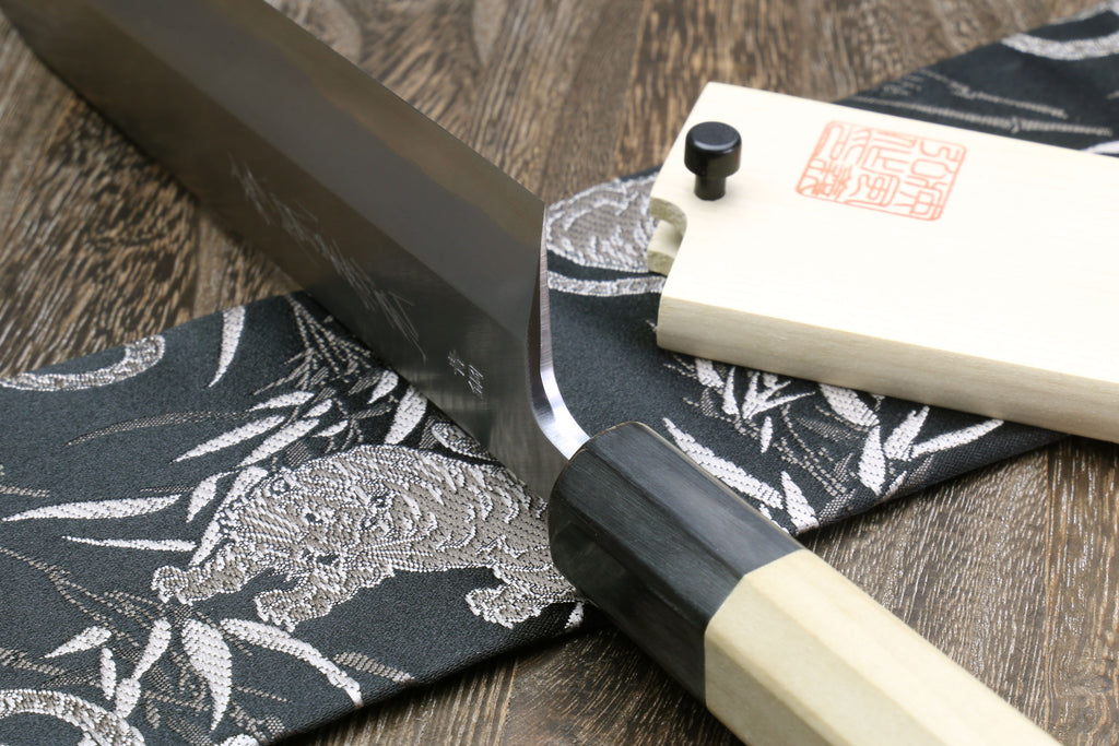 Eel filet knife handle detail with dark collar and pale saya on patterned cloth
