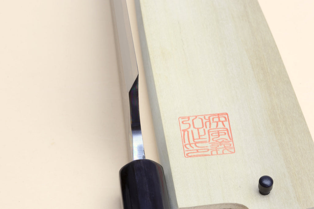Knife handle close-up with dark grip panel and red stamp on pale wood