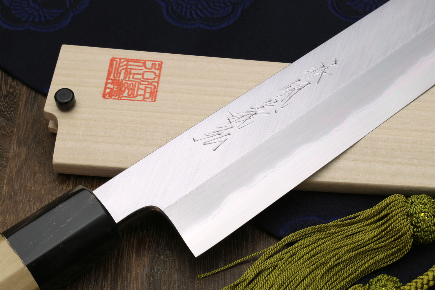 Japanese chef knife with white steel blade close-up and magnolia handle, green tassel cord.
