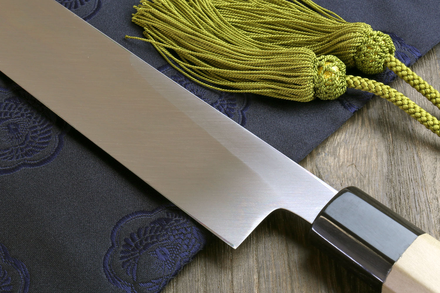 Japanese chef knife with white steel blade and dark butt, magnolia handle, green tassel cord.