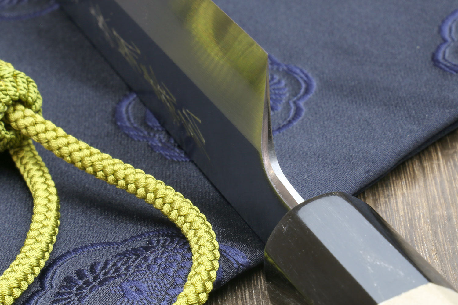 Japanese chef knife tip close-up with white steel blade and magnolia handle, green tassel cord.