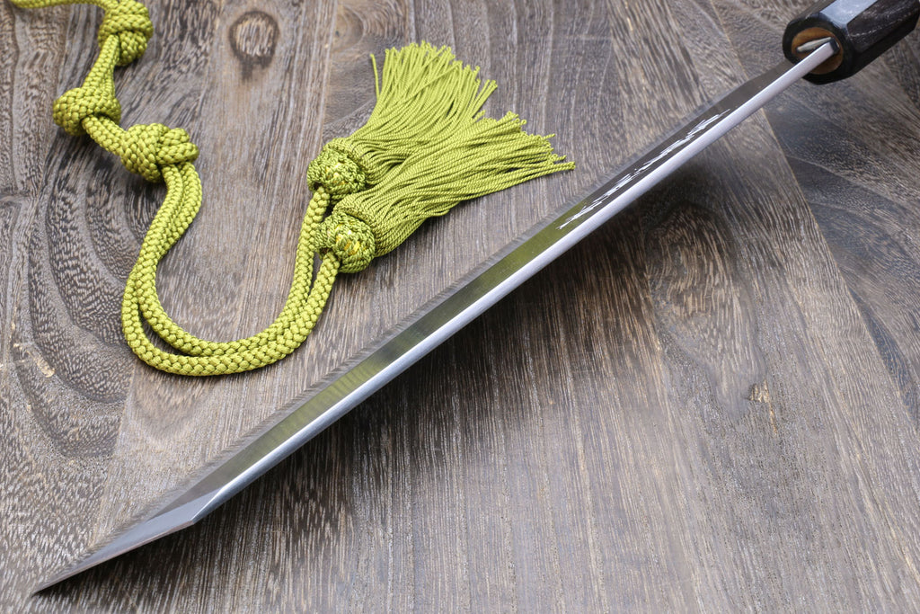 Japanese chef knife with white steel blade and magnolia handle, laid on green tassel cord.