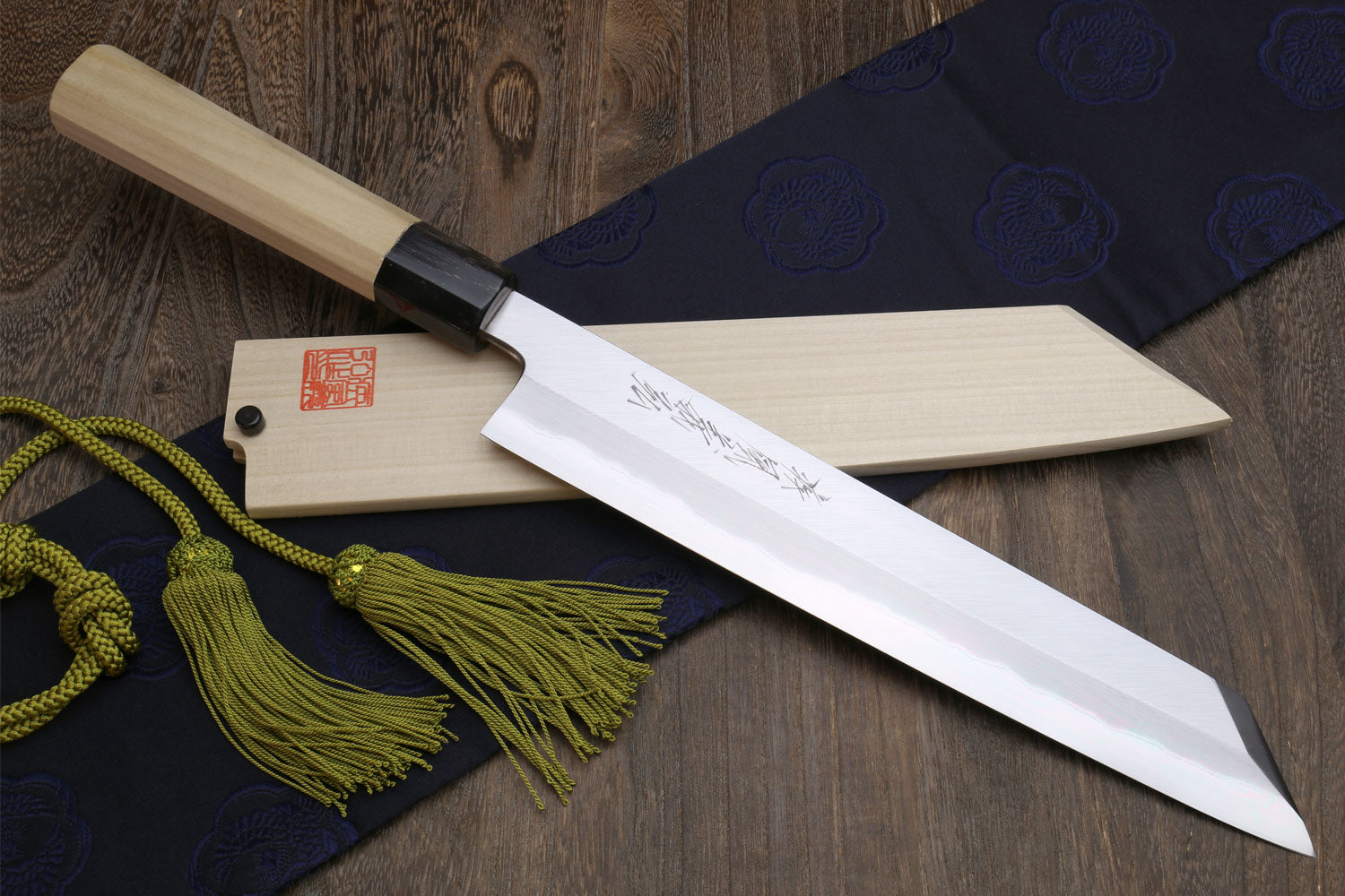 Japanese chef knife with white steel blade and magnolia handle, wooden sheath and green tassel cord.