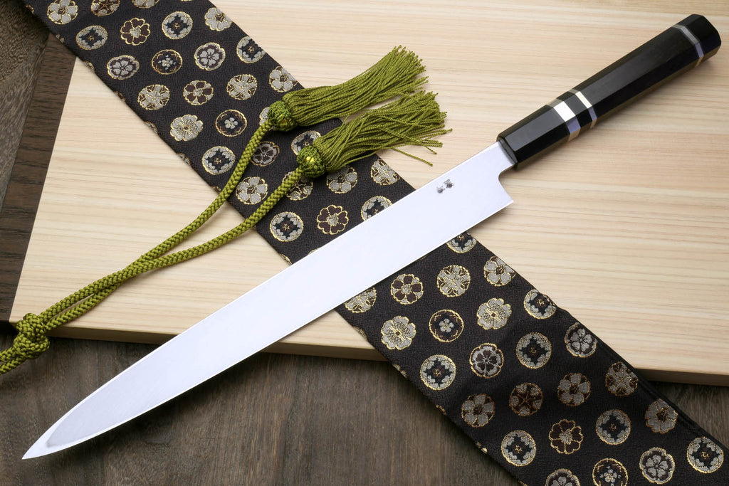 Yanagi sushi knife with dark handle, mirror silver blade, and green tassel cord on patterned cloth