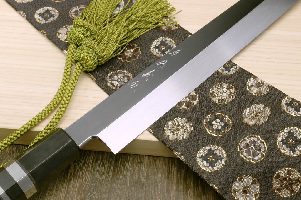 Yanagi sushi knife with mirror silver blade and dark handle, paired with green cord tassel