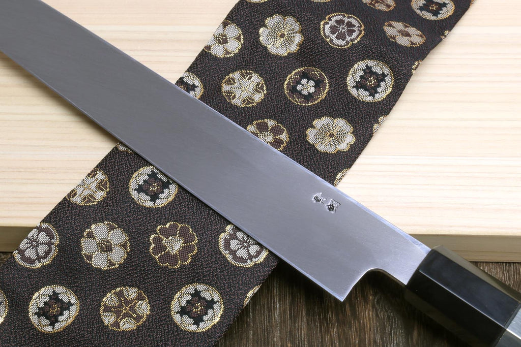 Yanagi sushi knife with mirror-finished silver blade and dark handle on patterned fabric