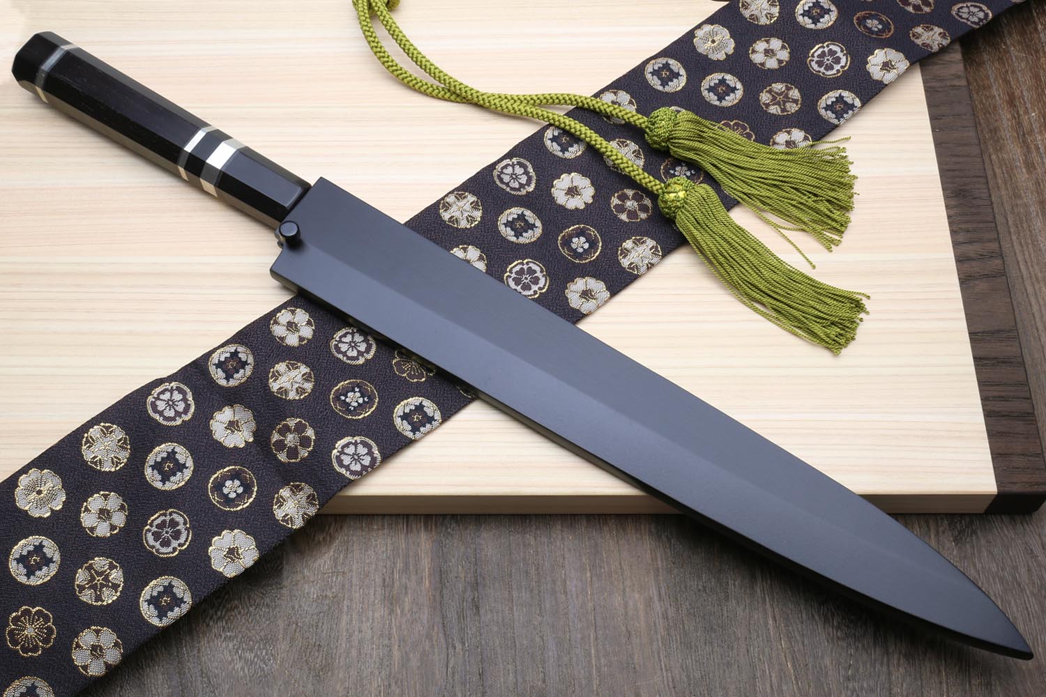 Yanagi sushi knife with dark handle and mirror silver blade on patterned cloth with green tassel