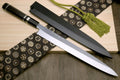 Yanagi sushi knife with mirror silver blade and dark handle, shown with black sheath