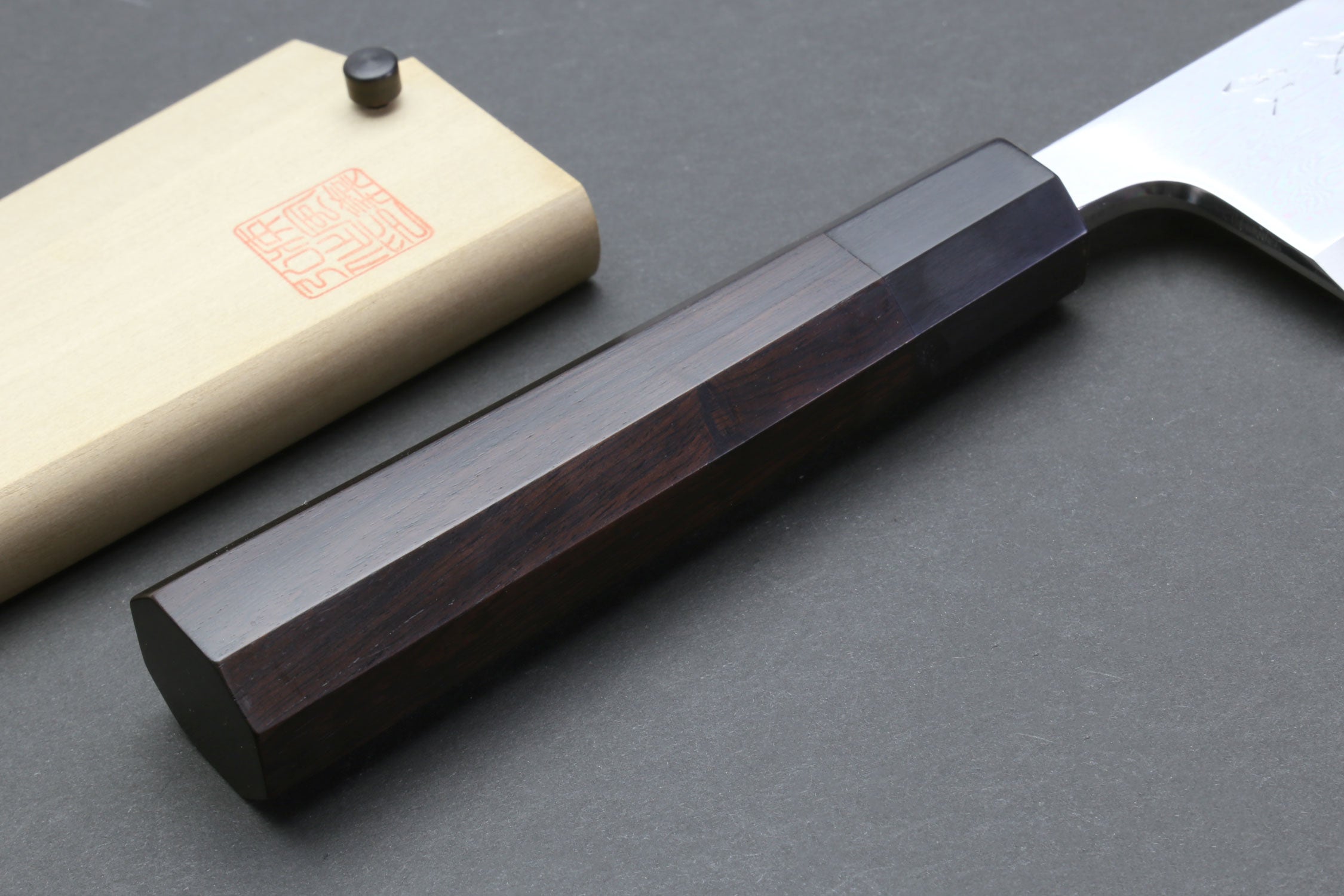 Deba sushi fillet knife with dark handle and light wooden saya on wood support