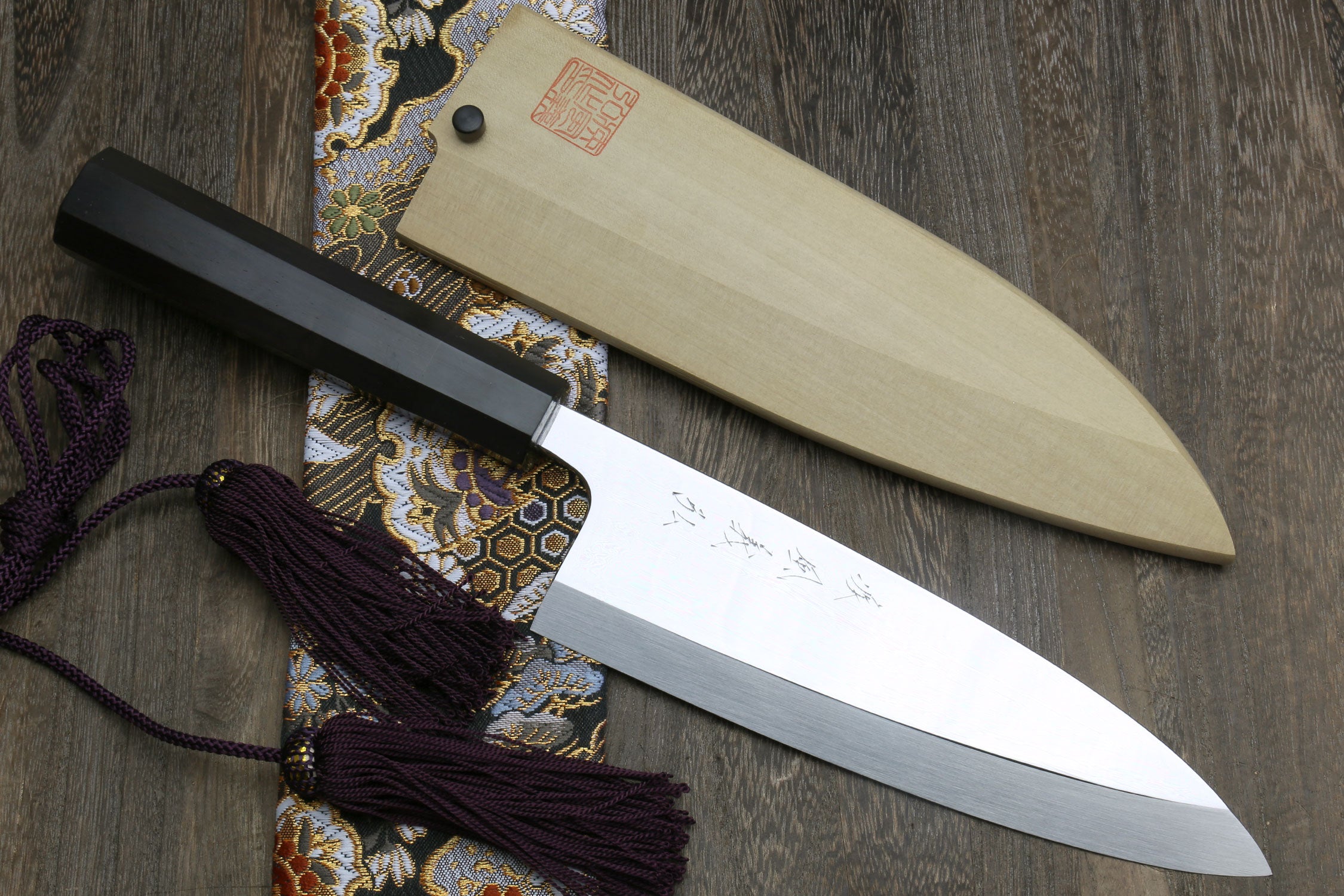 Mirror-finished deba sushi fillet knife with dark handle and light wooden saya