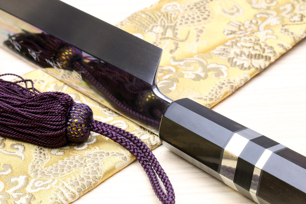 Japanese yanagiba sushi knife close-up: mirror-finished blade, black handle, silver striped bands