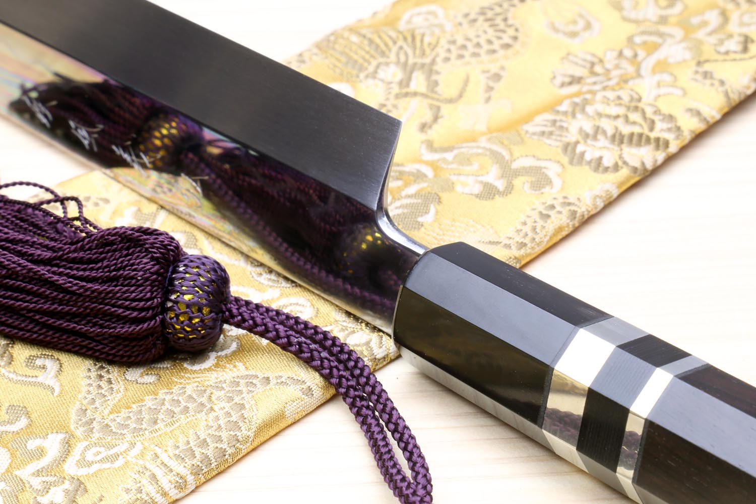 Japanese yanagiba sushi knife close-up: mirror-finished blade, black handle, silver striped bands