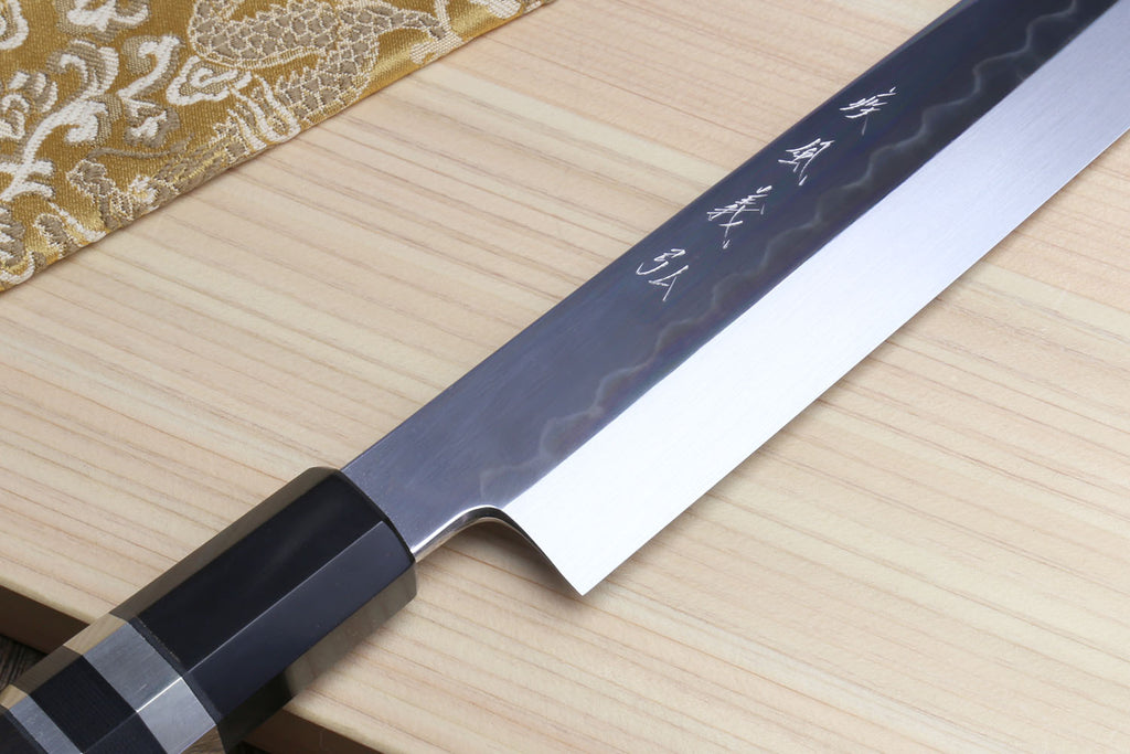 Japanese yanagiba sushi knife blade and bolster with etched pattern; black handle with silver bands