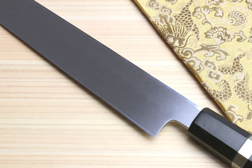 Japanese yanagiba sushi knife blade close-up with smooth mirror finish and black handle with silver bands