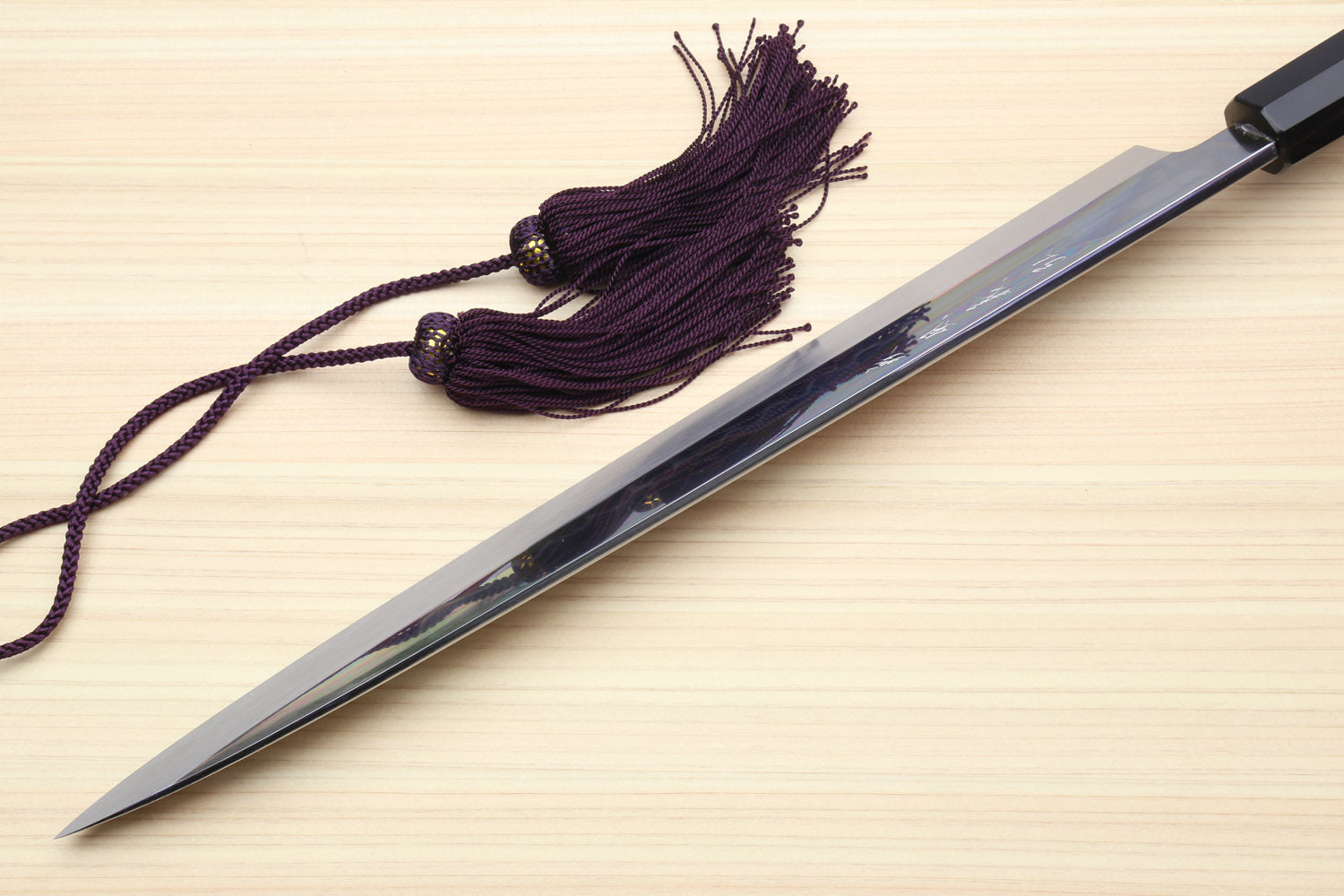 Japanese yanagiba sushi knife side view on wood with black cord tassel and striped handle bands