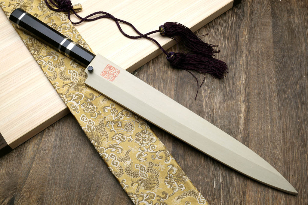 Japanese yanagiba sushi knife on wooden board with black handle bands and tassel cord