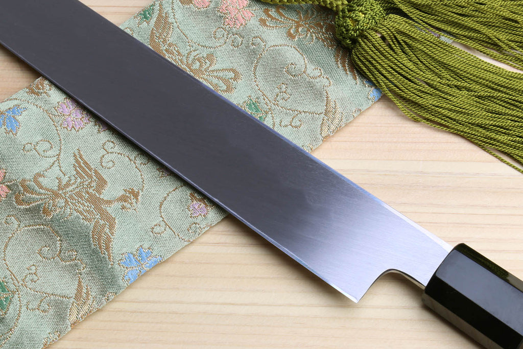 Japanese sashimi knife with dark bolster and mirror-finished blade on wooden board