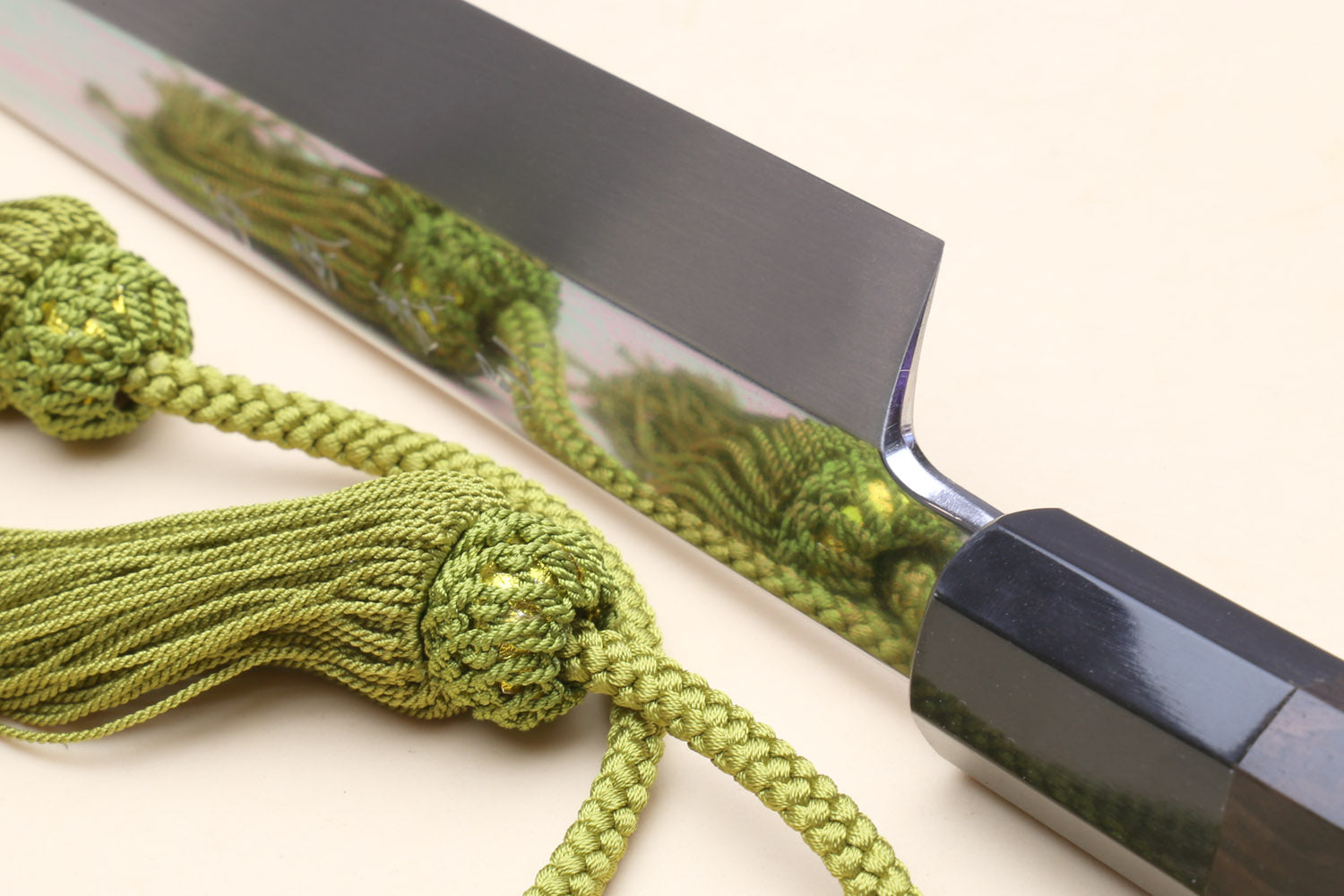 Yanagi knife with mirror-finished blade and dark handle, green cord and tassel detail.