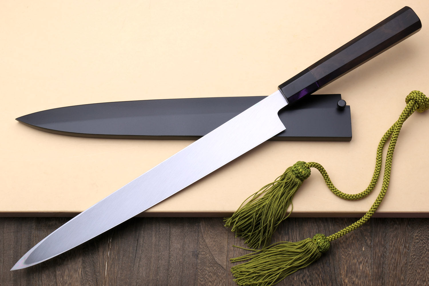 Yanagi knife with mirror-finished steel blade and dark handle, with green cord tassels.
