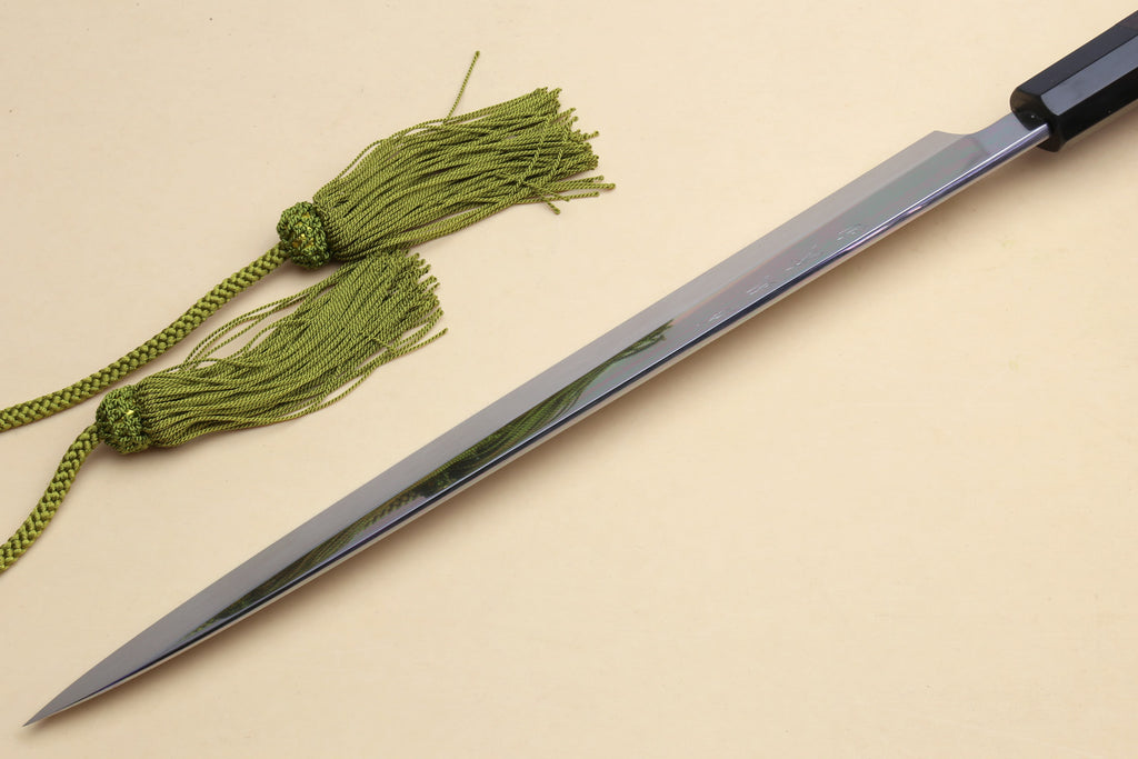 Yanagi knife with pointed mirror blade and dark handle, green cord tied nearby.