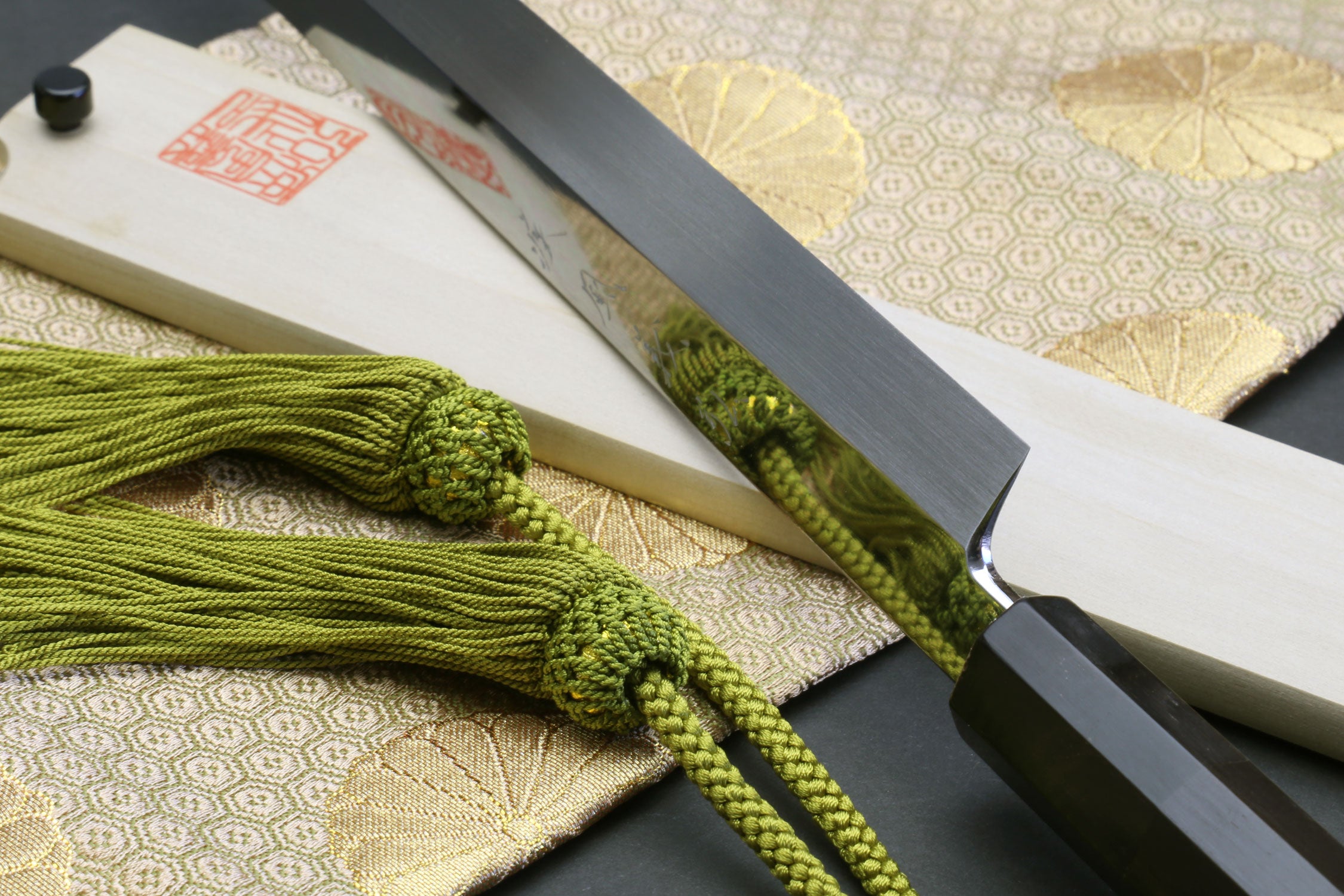 Sushi chef knife with mirror-finished blade, dark spine, and ebony handle close-up.